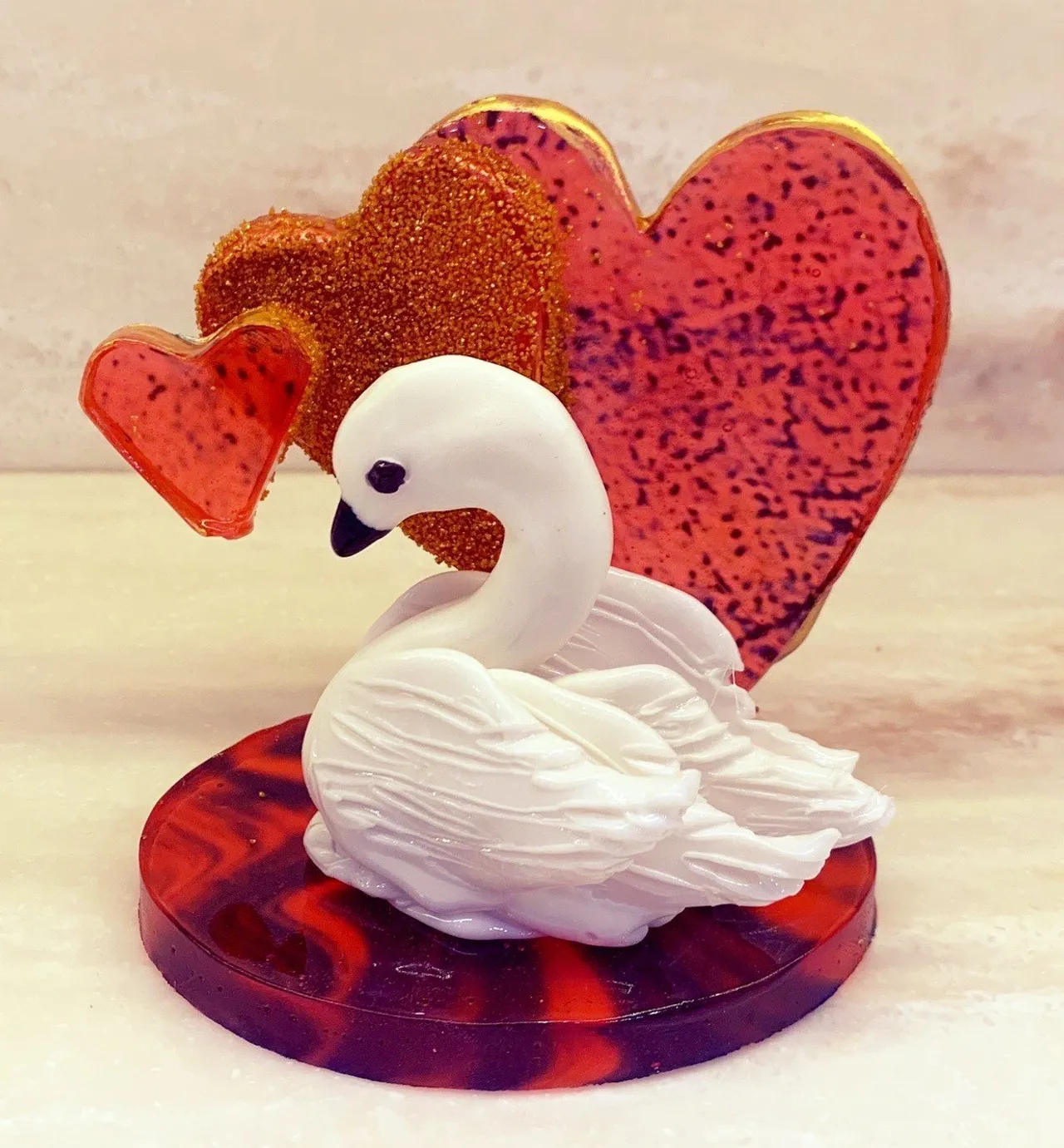 An isomalt sugar swan figurine on a marbled red and purple base with heart decorations