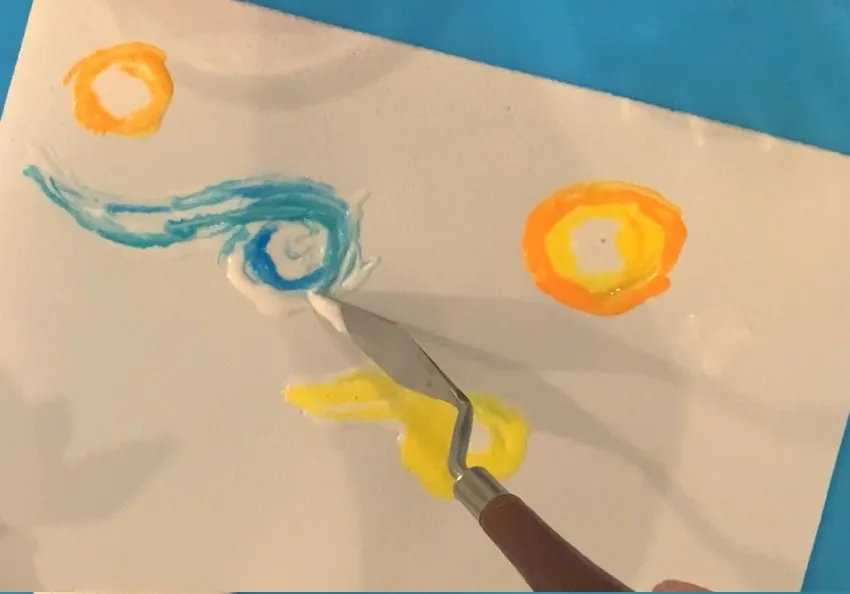 Palette knife swirling blue, yellow, and orange edible colors on paper.