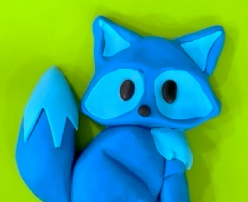 Blue fondant fox figurine with black eyes, nose, and white tail tuft.