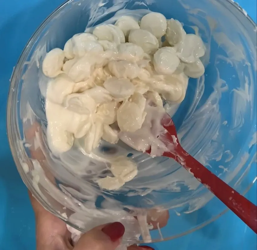 Hand tempering white chocolate in a glass bowl with a spatula.