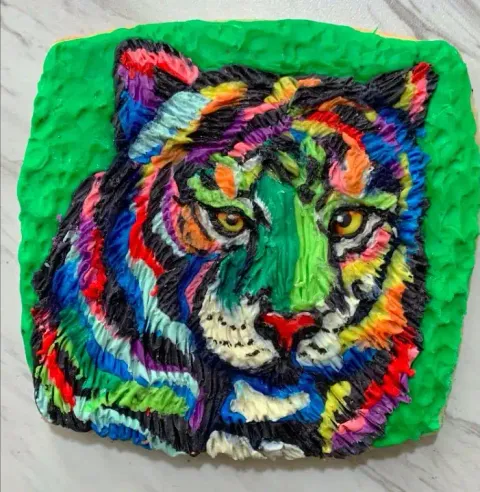 A modeling chocolate tiger face with rainbow-colored fur stripes and yellow eyes on a green background
