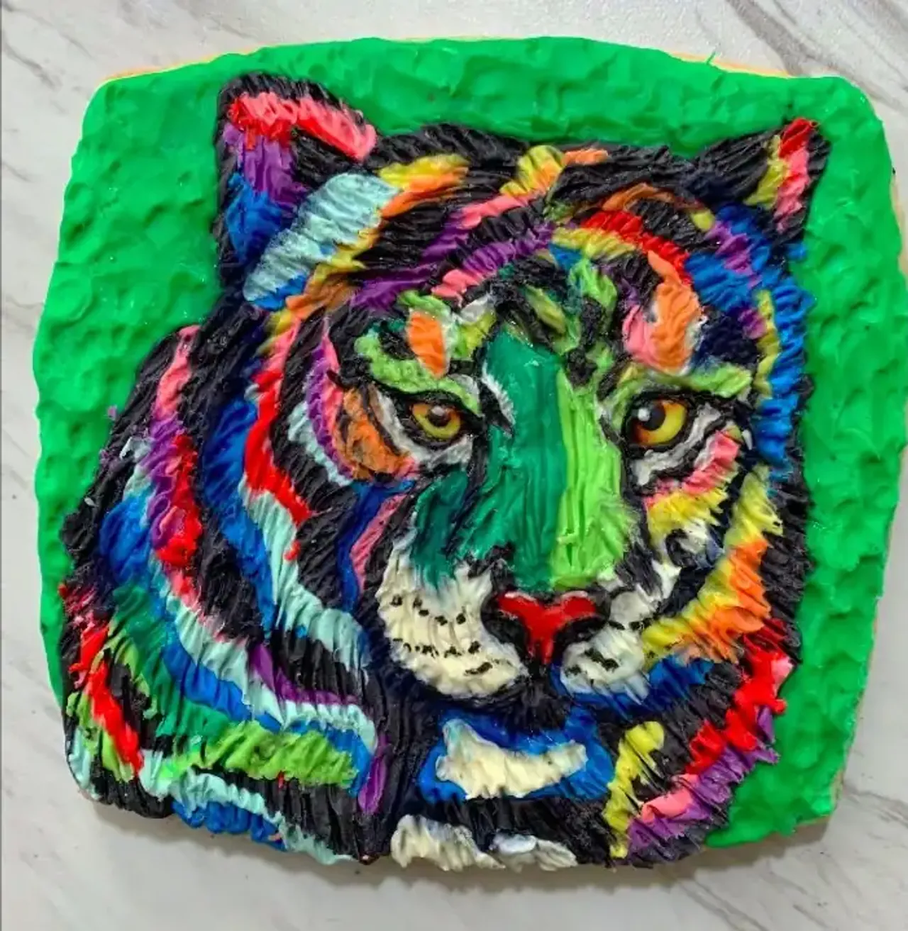 A modeling chocolate tiger face with rainbow-colored fur stripes and yellow eyes on a green background