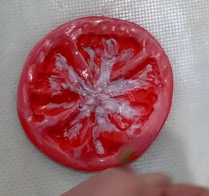 A red fondant tomato slice with detailed interior on a cutting mat.