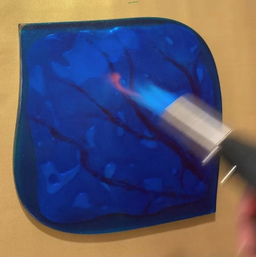 Close-up of blue isomalt being heated with a blowtorch to remove air bubbles.