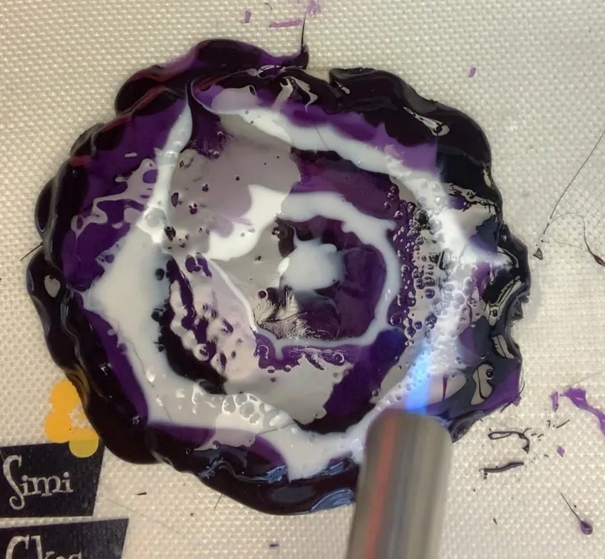 Using a torch to pop bubbles in the melted isomalt geode on the cookie.