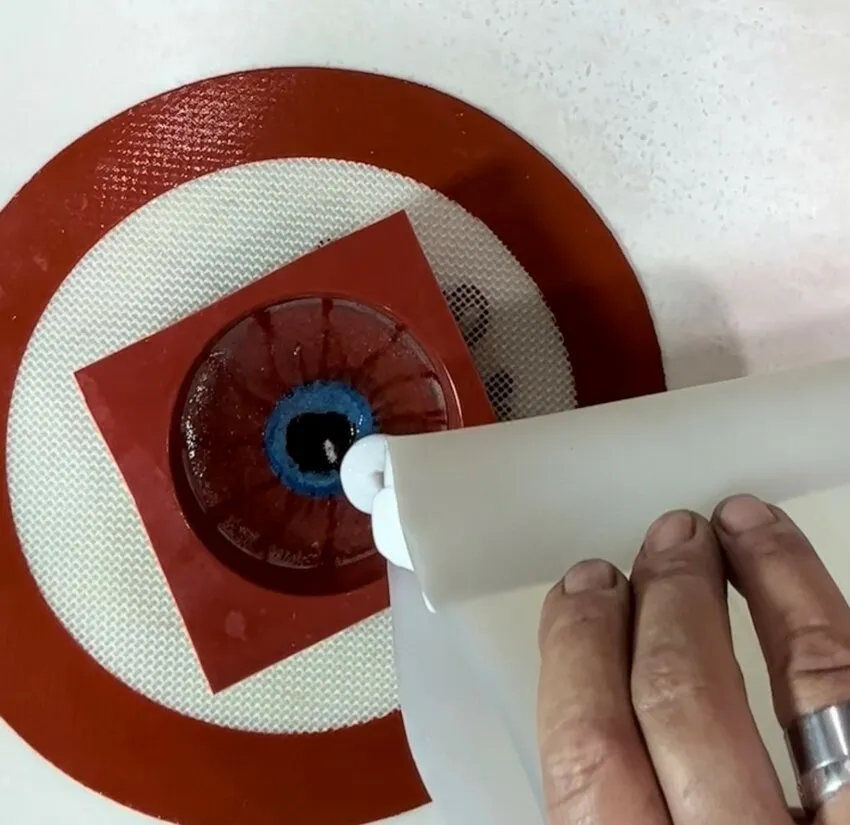 White isomalt being poured onto the back of the eyeball in the mold.
